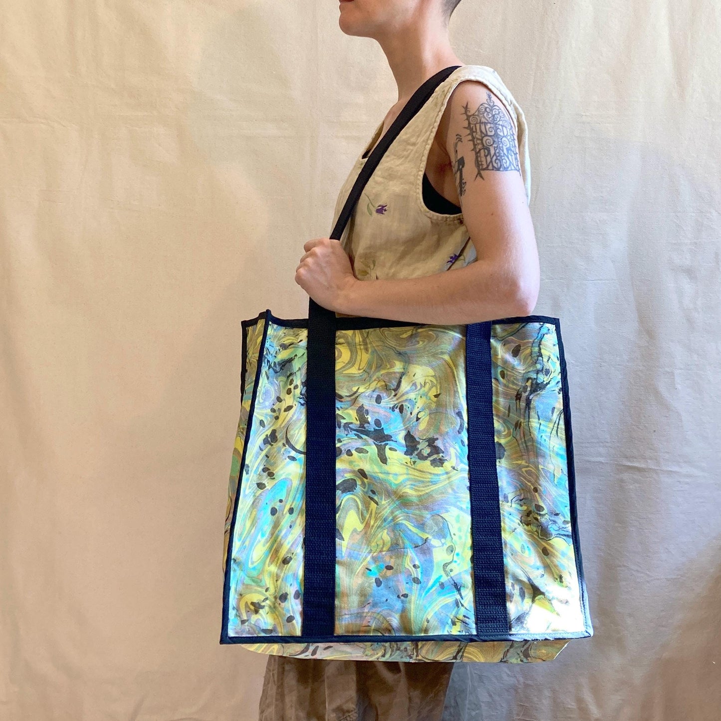 A person modelling an oversized water marbled tote bag with contrasting straps