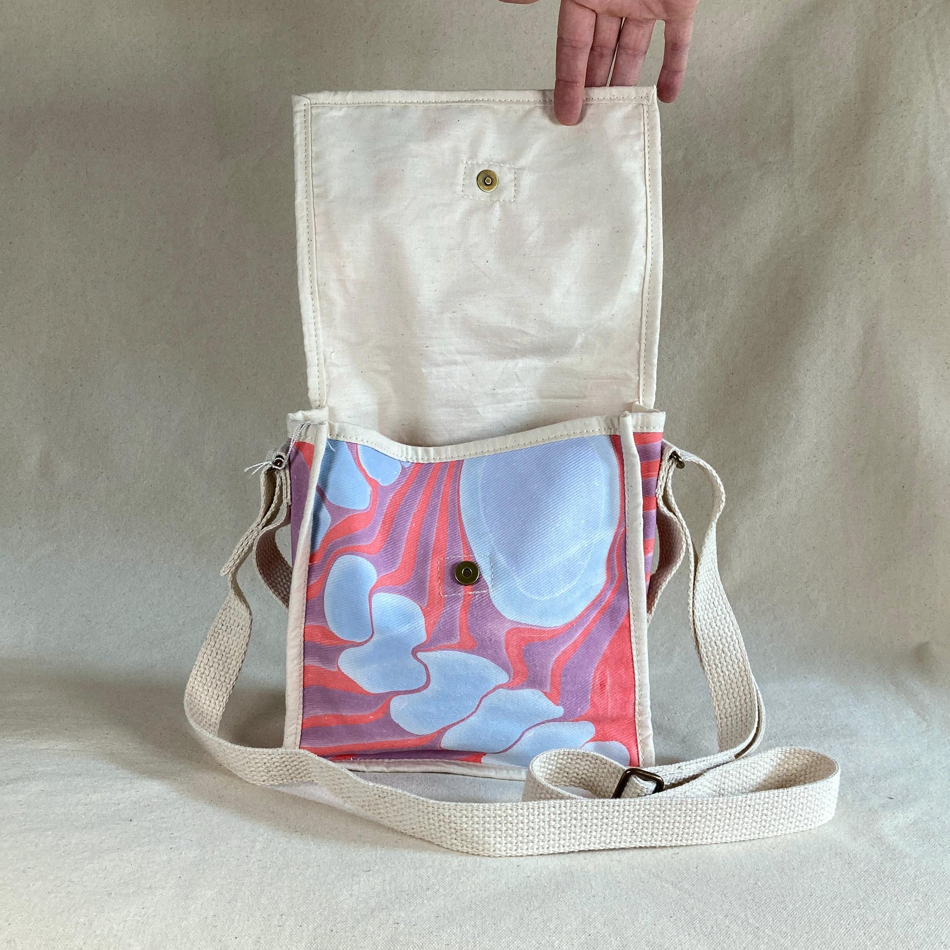 A mini square water marbled messenger bag with a flap open to show snap closures